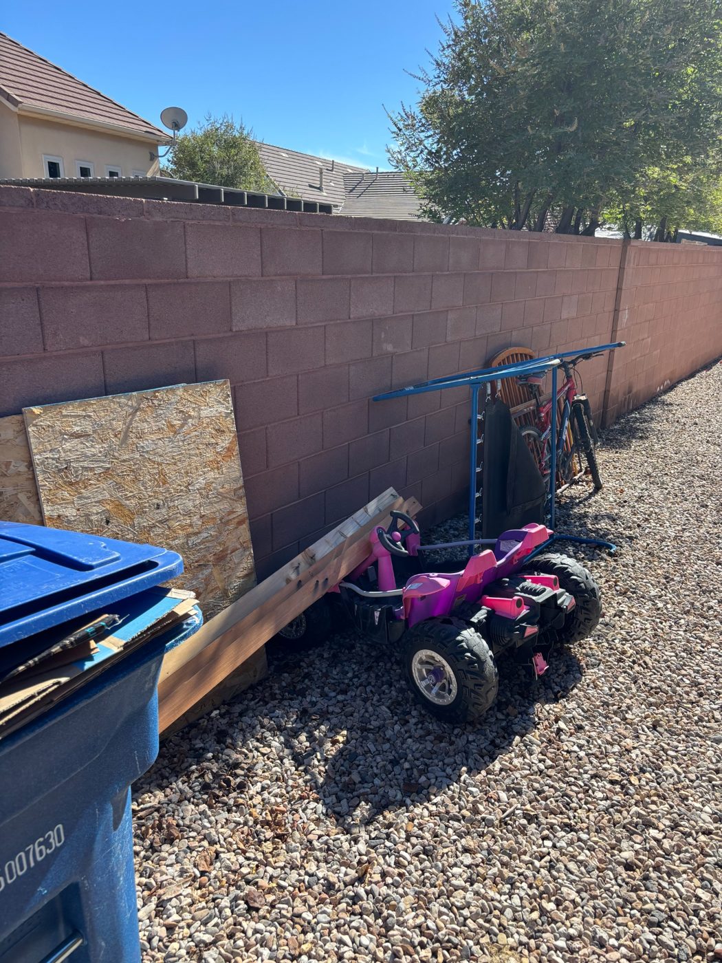 Before junk removal: scrap wood, small toys and other items along a backyard block wall